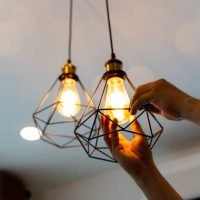 istockphoto-1472464806-612×612 Electric LED Lightbulb Change In Light At Home. Decorative antique edison style filament light bulbs hanging. An electrician is installing spotlights on the ceiling